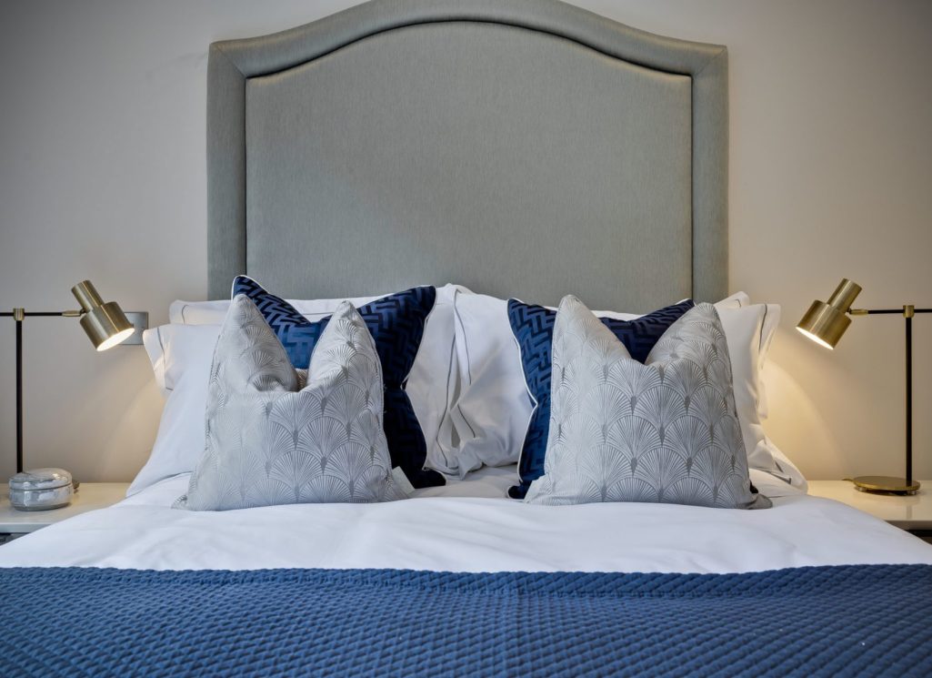 Symmetrical modern bedroom design by Curated Chaos Interiors featuring a curved grey headboard, navy blue textured cushions