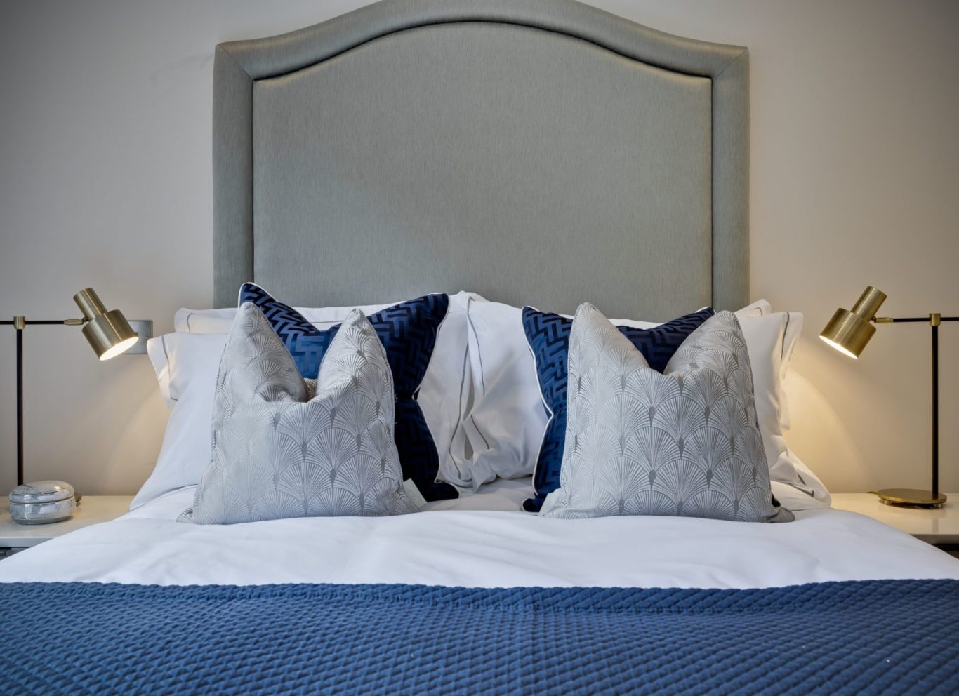 Symmetrical modern bedroom design by Curated Chaos Interiors featuring a curved grey headboard, navy blue textured cushions